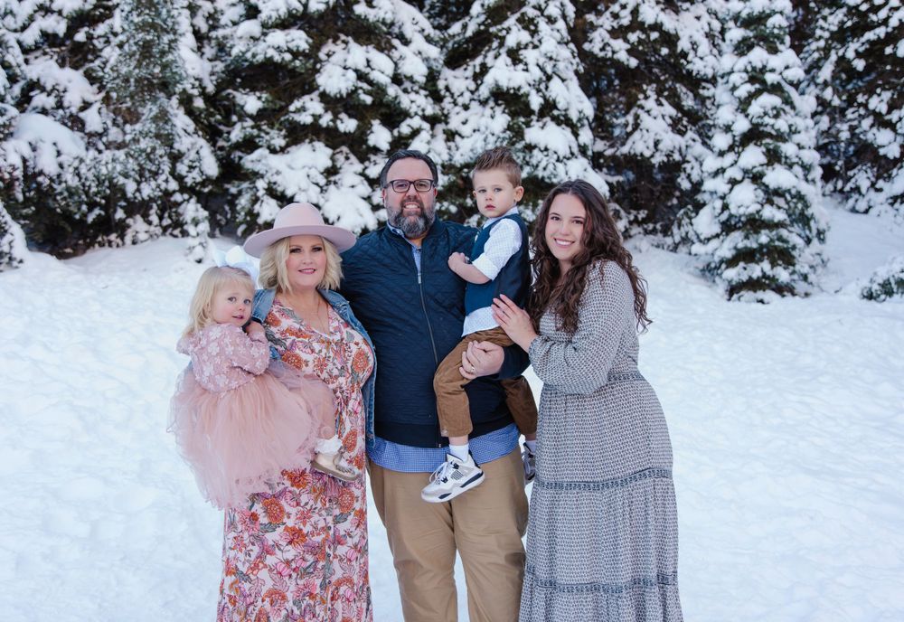 A winter family portrait with snow-covered pine trees creating a magical backdrop.