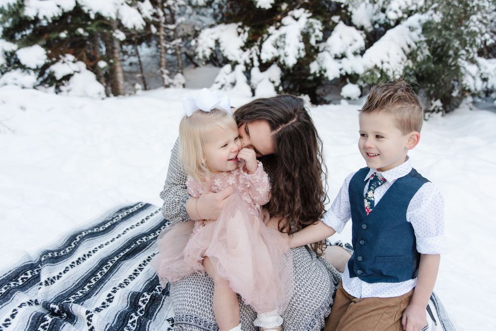 Family sitting on blanket in snowy winter setting sharing an intimate moment together.