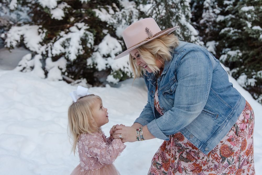 Two people share a tender winter moment in the snow surrounded by evergreen trees.