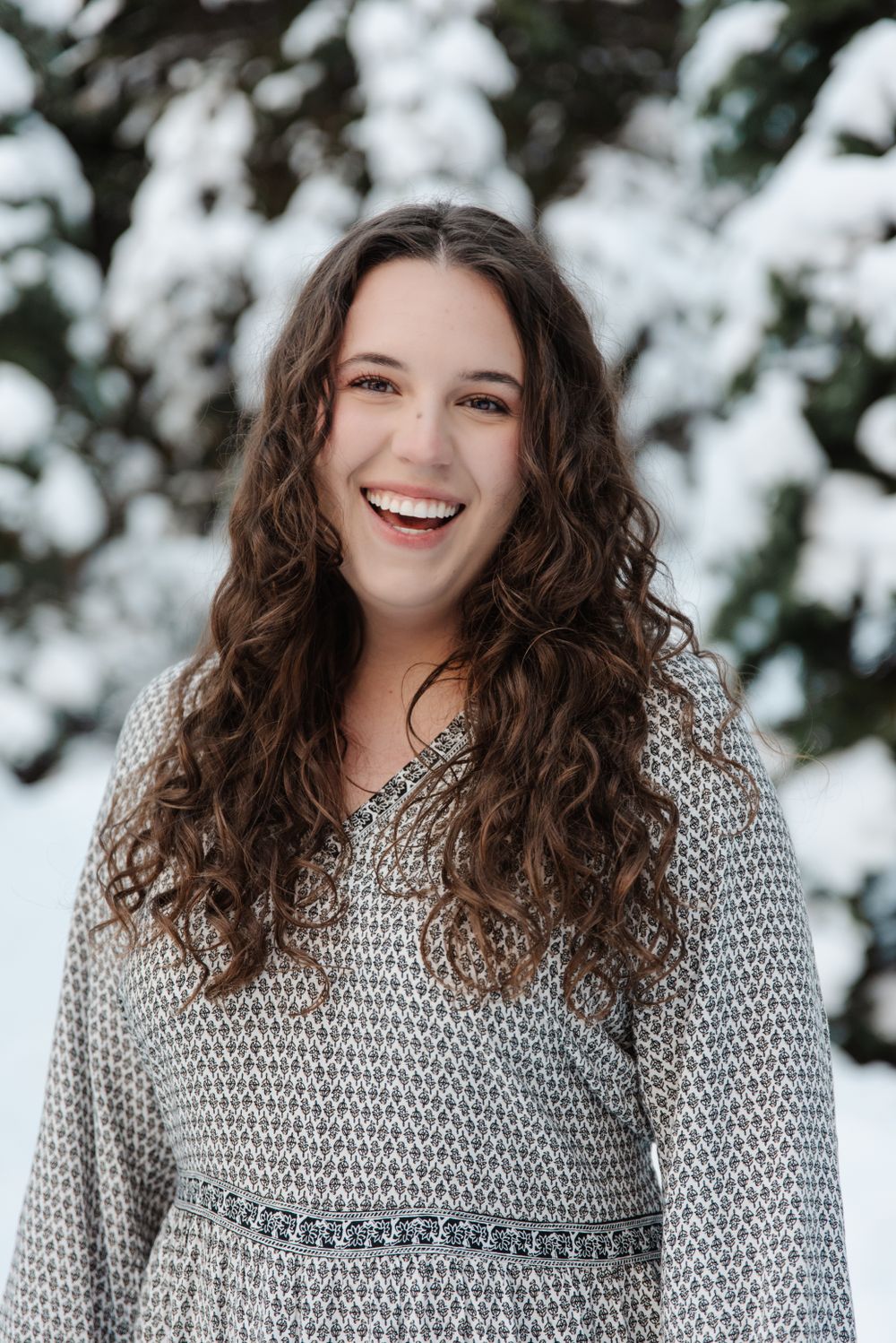 Portrait of woman in gray sweater smiling against snowy winter background.