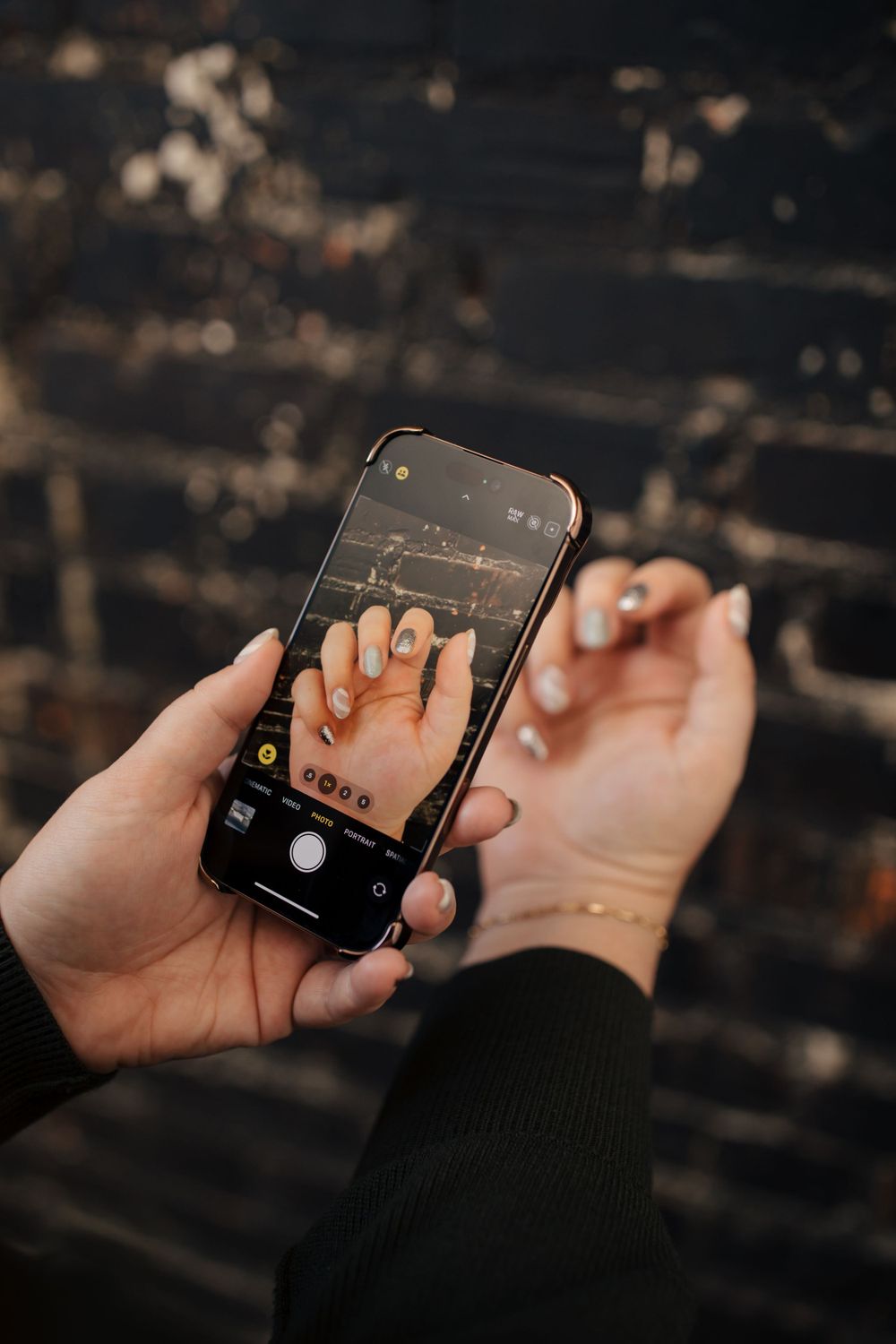 Someone taking a photo of their hand with an iPhone camera against a dark wooden background.