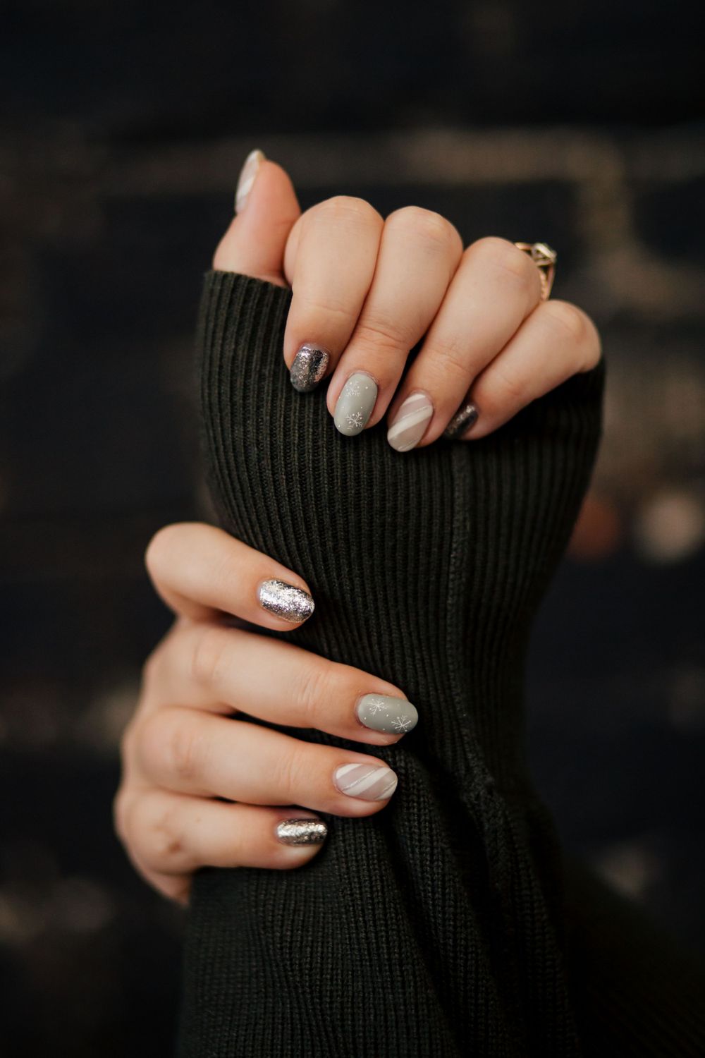 Close up of hands with silver and grey sparkly manicured nails wearing a black ribbed sweater sleeve.