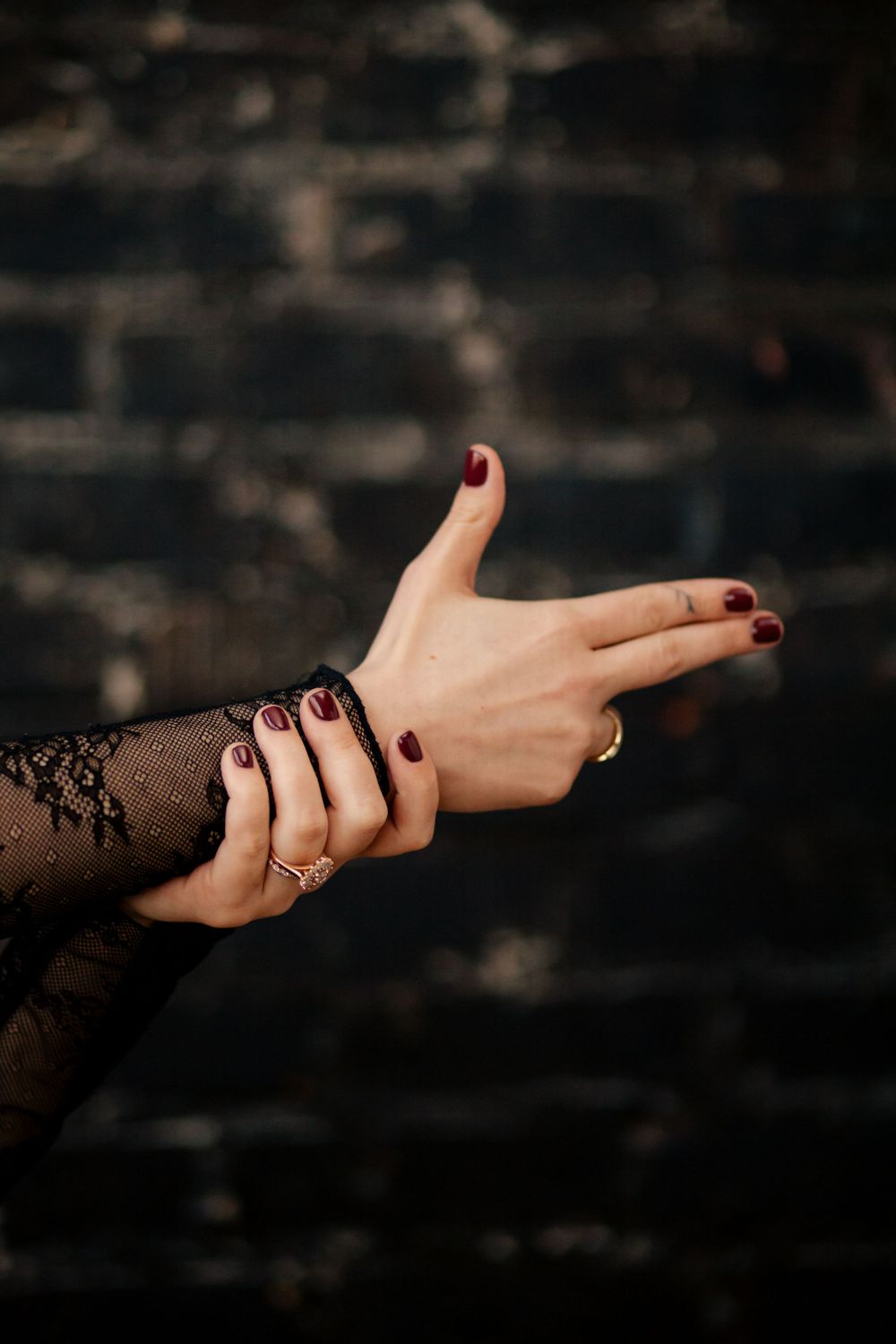 Female hand with dark burgundy nail polish and lace sleeve detail extends against a dark textured background.