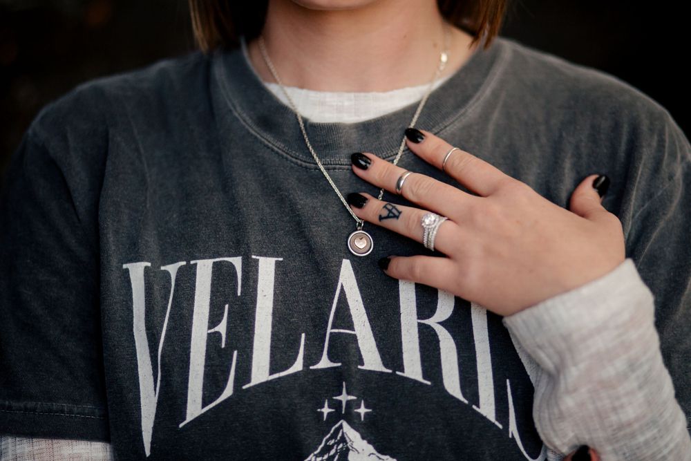 Close-up of a hand with black nail polish touching a sweatshirt with 'VELARIS' text printed on it.