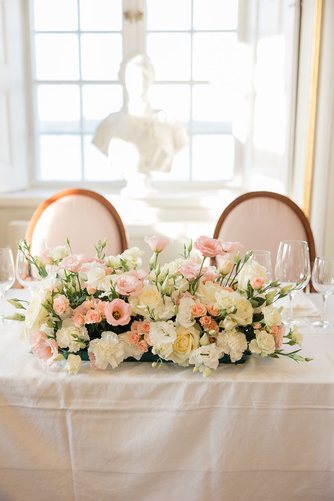 Elegant floral centerpiece arrangement of pink and white flowers on long white tablecloth at wedding reception.