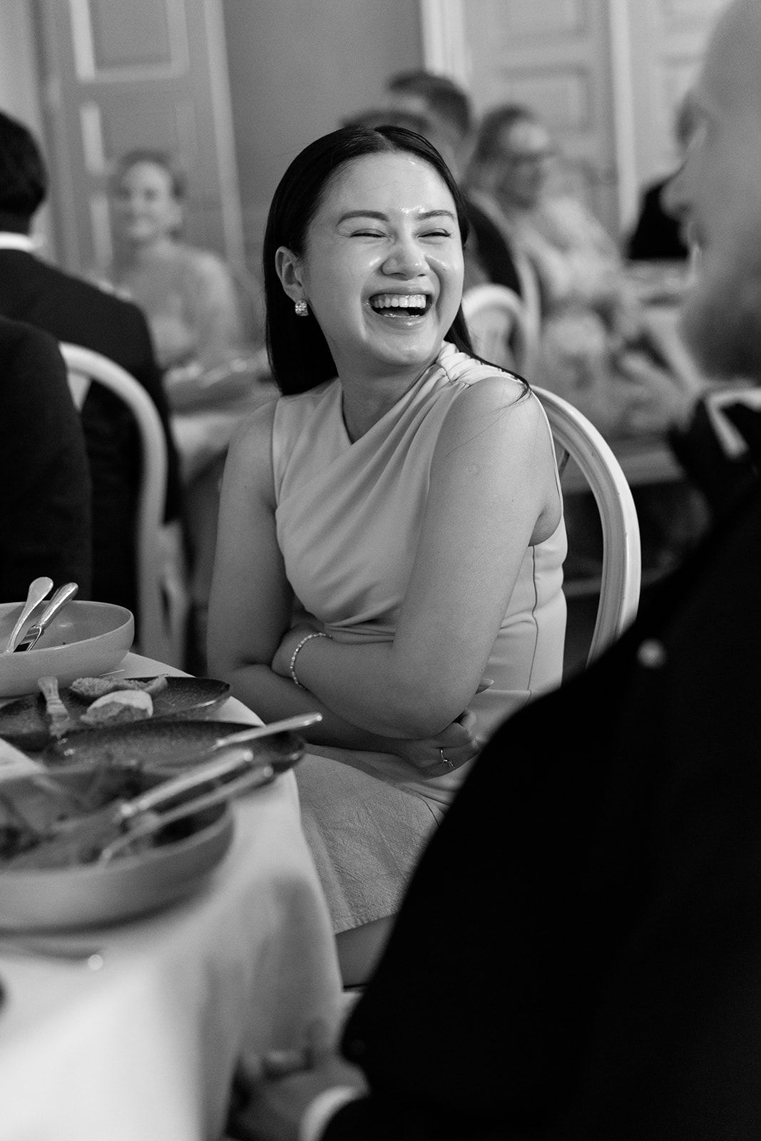 A series of four black and white photos showing someone laughing joyfully at a dining table.