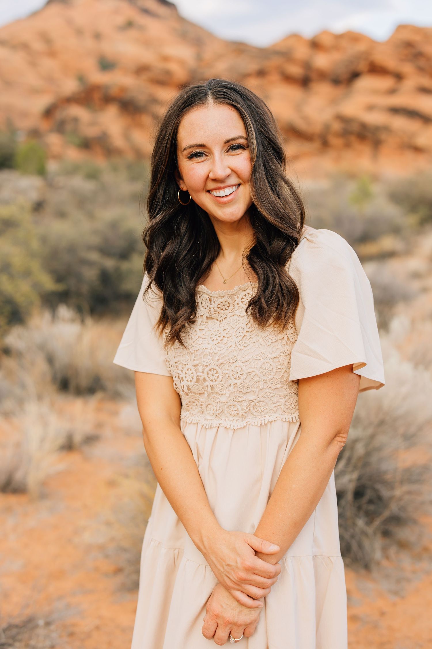 Portrait of person in cream lace dress smiling against red rock desert background.