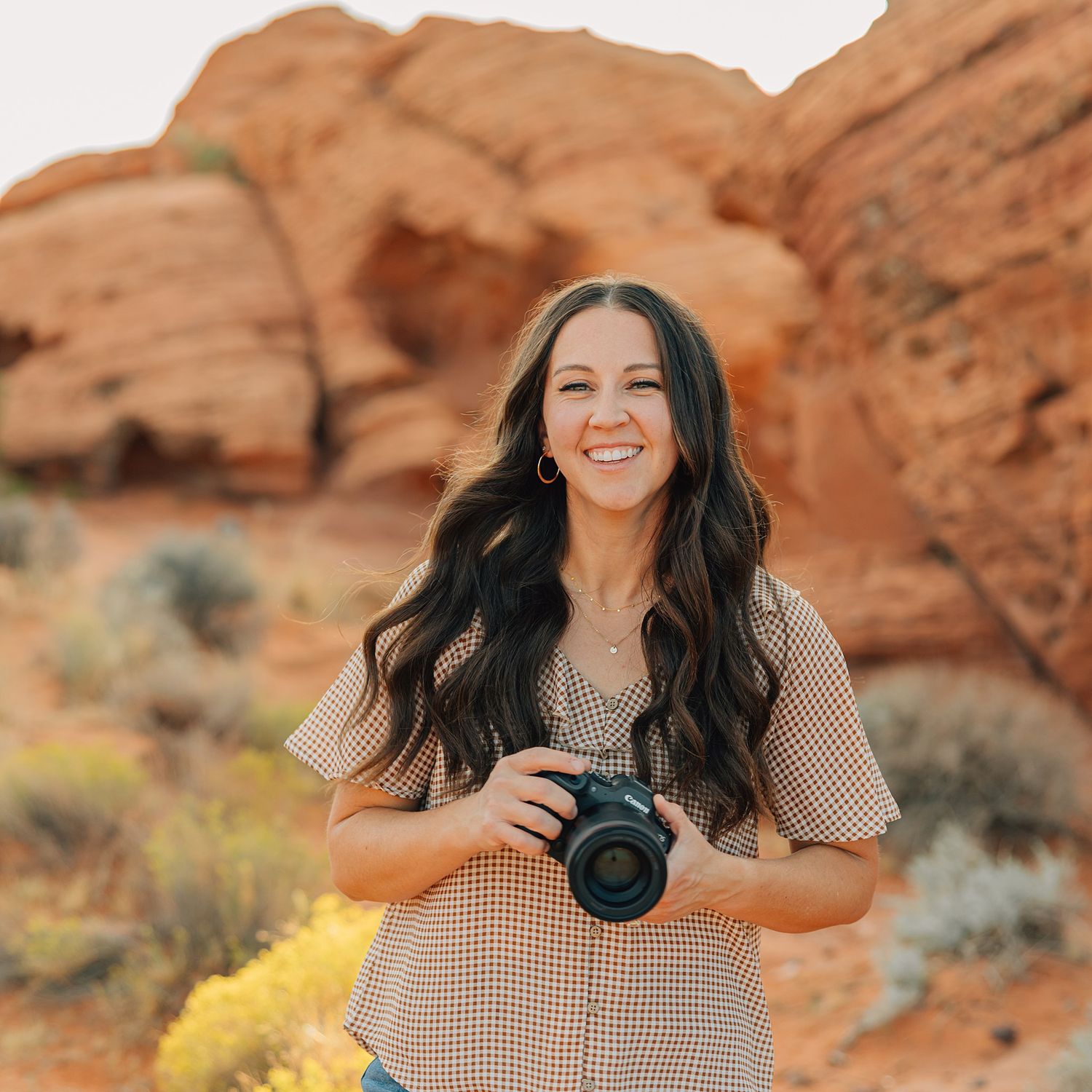 Portrait of person in cream lace dress smiling against red rock desert background.