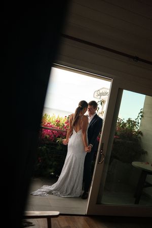 Silhouetted figures in wedding attire stand near a bright window with pink flowers visible outside.