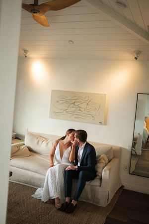 A couple in formal attire sitting together on a white sofa beneath abstract wall art.