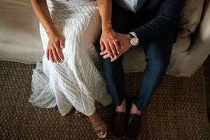 Close-up view of wedding dress details with hands resting on knees showing elegant lace and fabric textures.