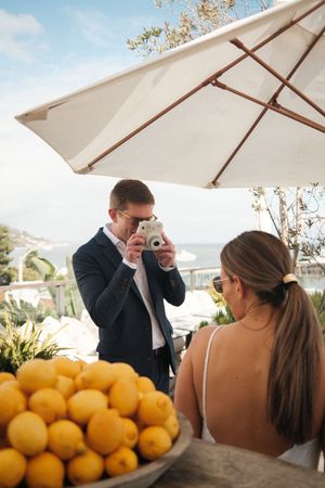 Citrus fruits and polaroid photos displayed on a table under white umbrellas at an outdoor event.