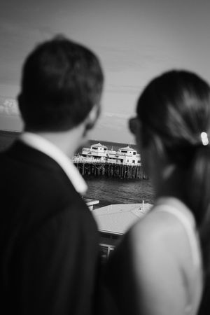 Black and white silhouette of couple looking at distant pier over water.