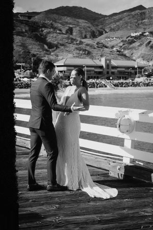 A romantic black and white scene of a couple on a wooden pier with mountains in the background.