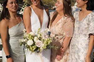 A bridal party in pastel and white dresses holding a bouquet of white and green flowers.
