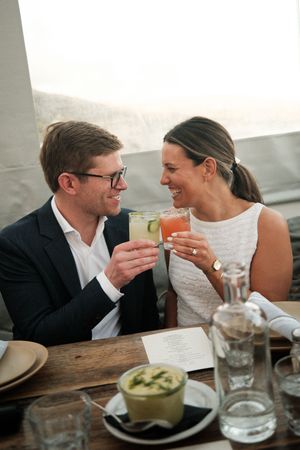 A couple shares intimate moments while dining at a restaurant table with drinks and plates visible.