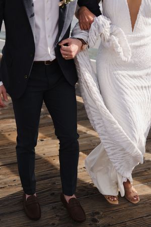 Close-up of formal attire showing a black suit and flowing white dress on wooden decking.