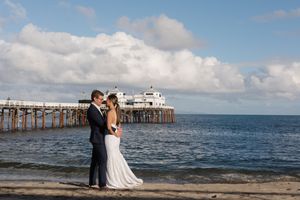 Scenic coastal wedding ceremony with a wooden pier and ocean waves in the background.