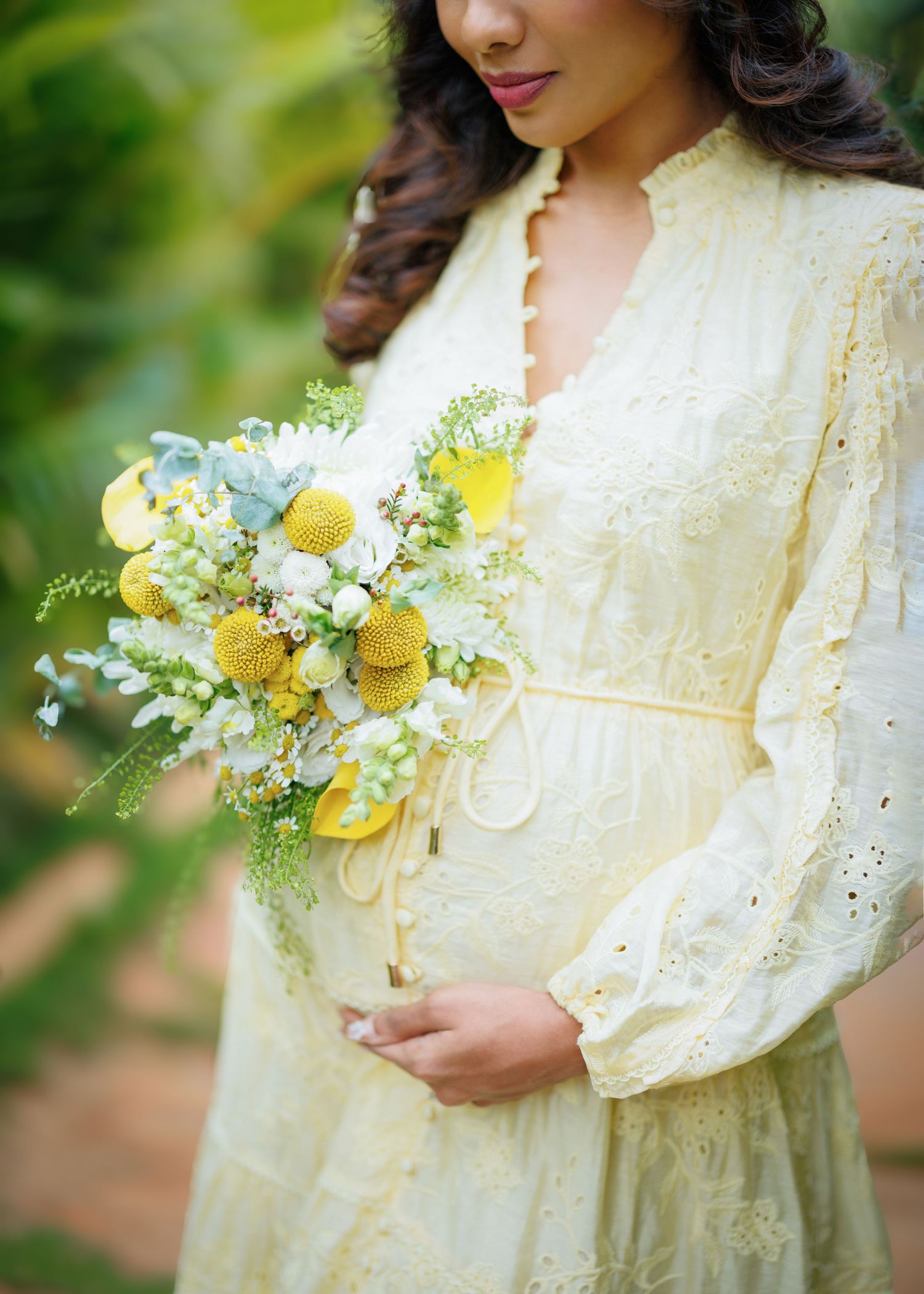 A delicate cream lace dress with bishop sleeves is paired with a romantic bouquet of yellow roses and white wildflowers.