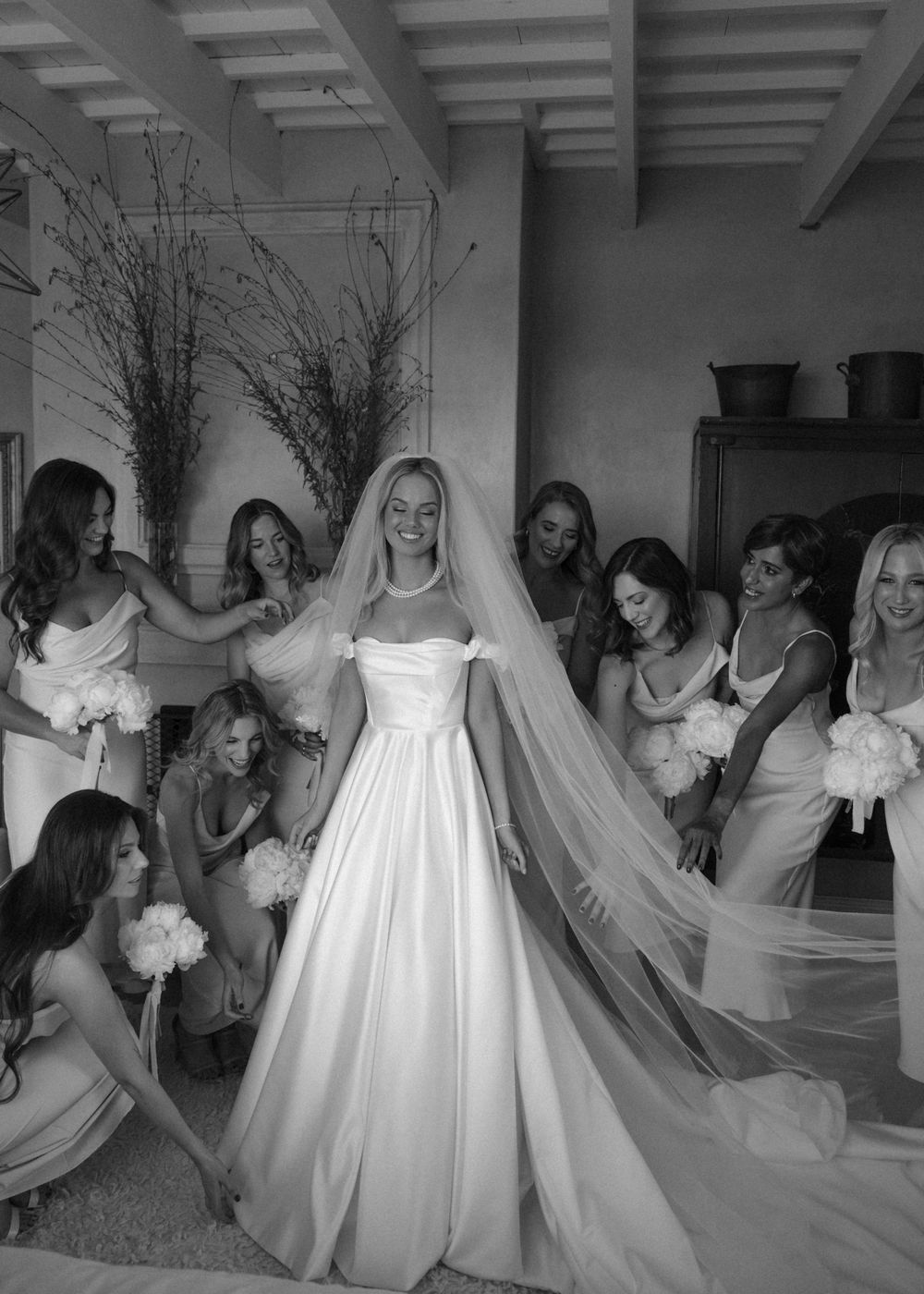 Multiple bridesmaids wearing white dresses pose together in a room.