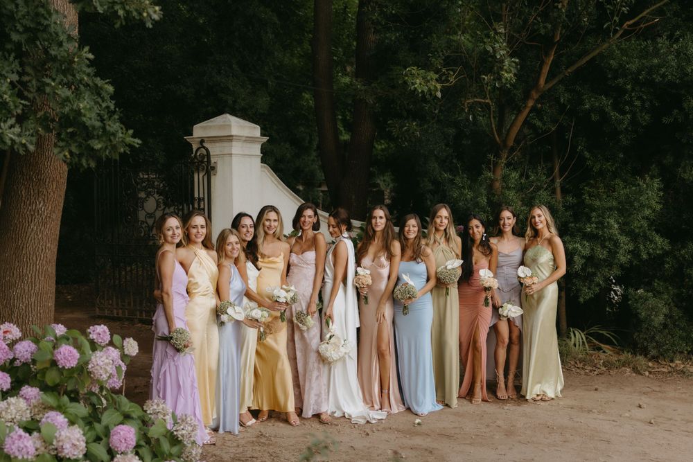 A group of people in pastel dresses stand in a line against a wooded background.