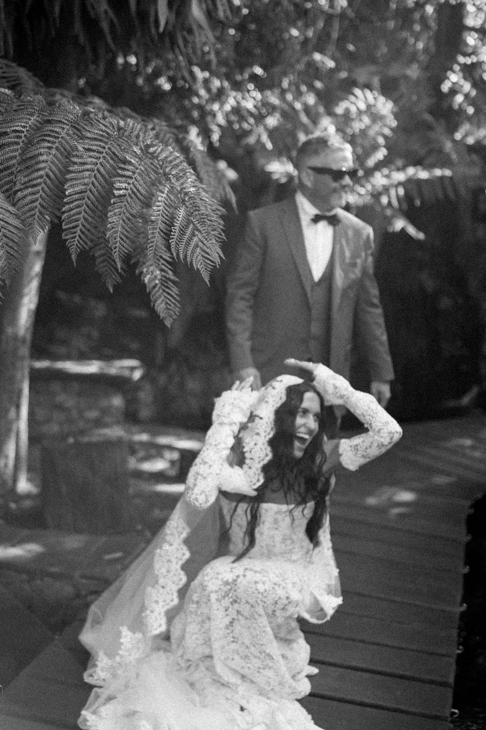 A black and white photograph showing a couple in formal wedding attire standing in a garden setting.