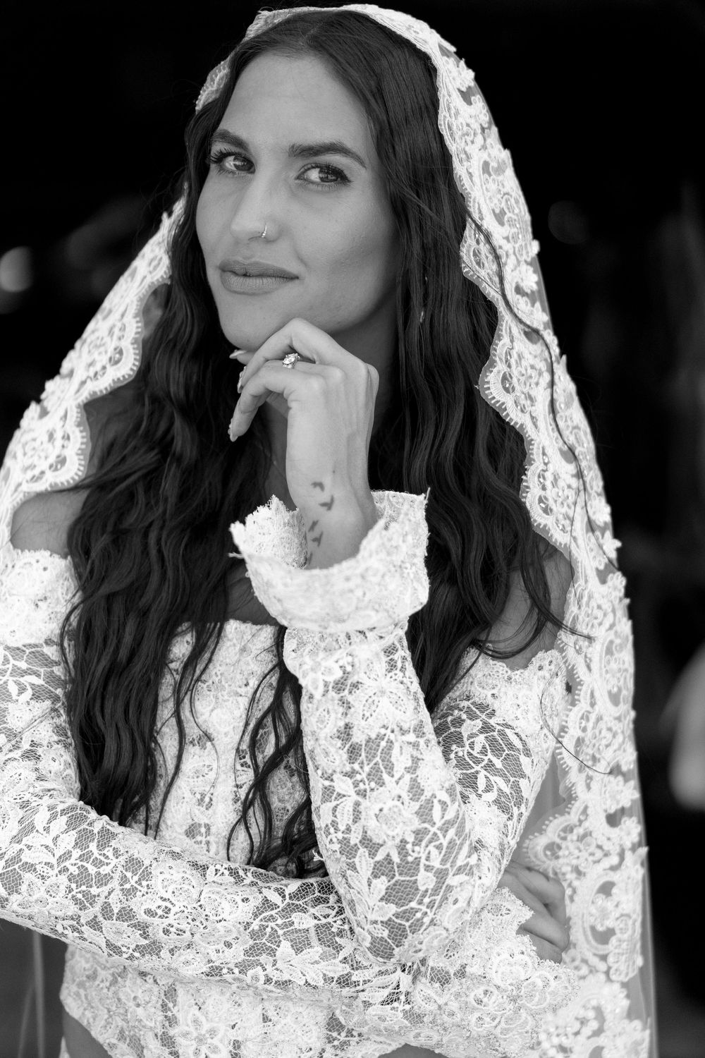 Black and white portrait of a bride wearing an elegant lace veil and dress with long dark wavy hair.