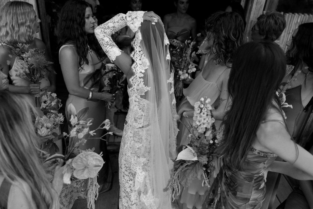 Black and white photo showing a wedding celebration with a bride in a lace veil surrounded by guests holding flowers.