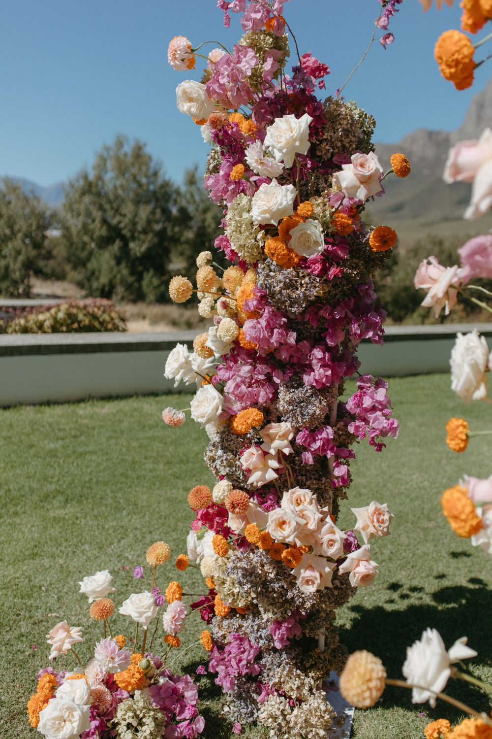Vibrant floral arch with pink, orange and white flowers against a sunny outdoor backdrop.