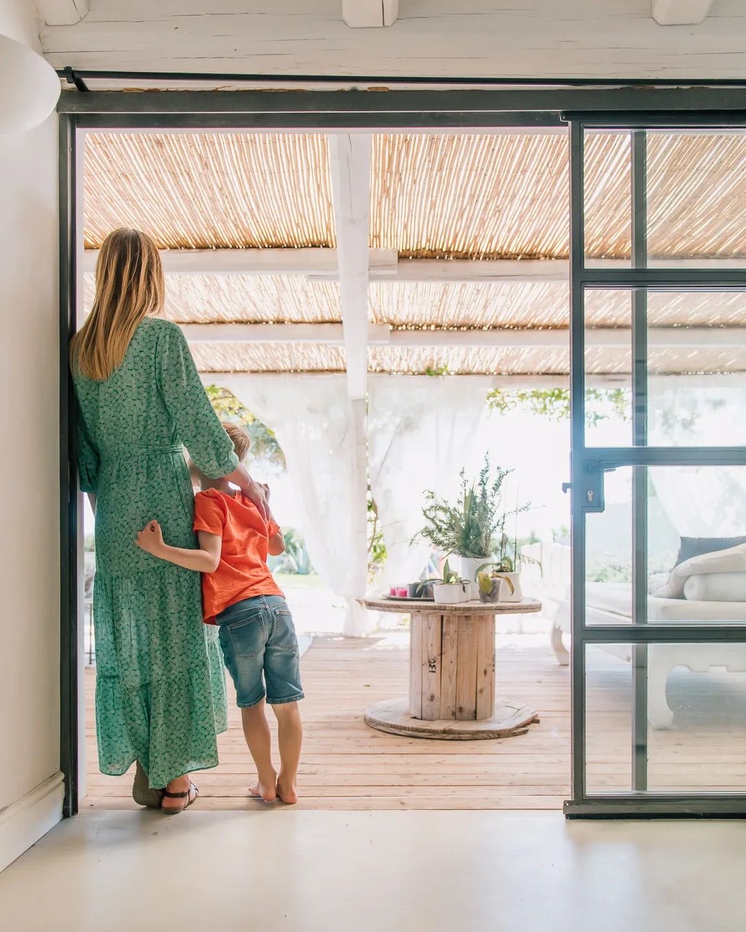 A mother and child stand by large glass doors in a bright home entryway filled with natural light.
