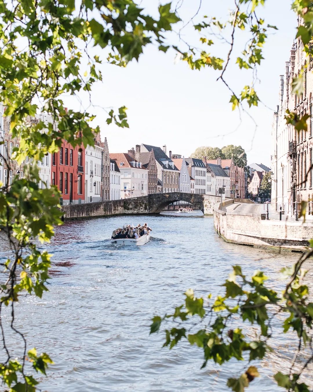 Small boats on a sunlit river lined with trees and historic buildings.