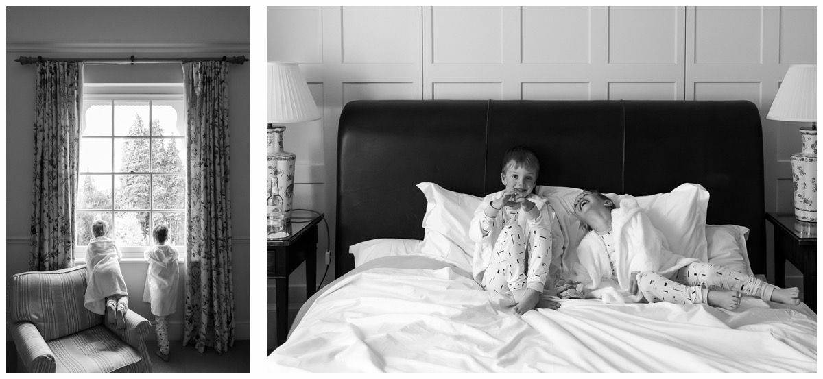 Children sitting on a neatly made hotel bed with open curtains and soft natural light filling the room.