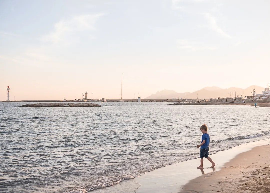 A child walking along the shoreline at sunset with calm waves and warm light.