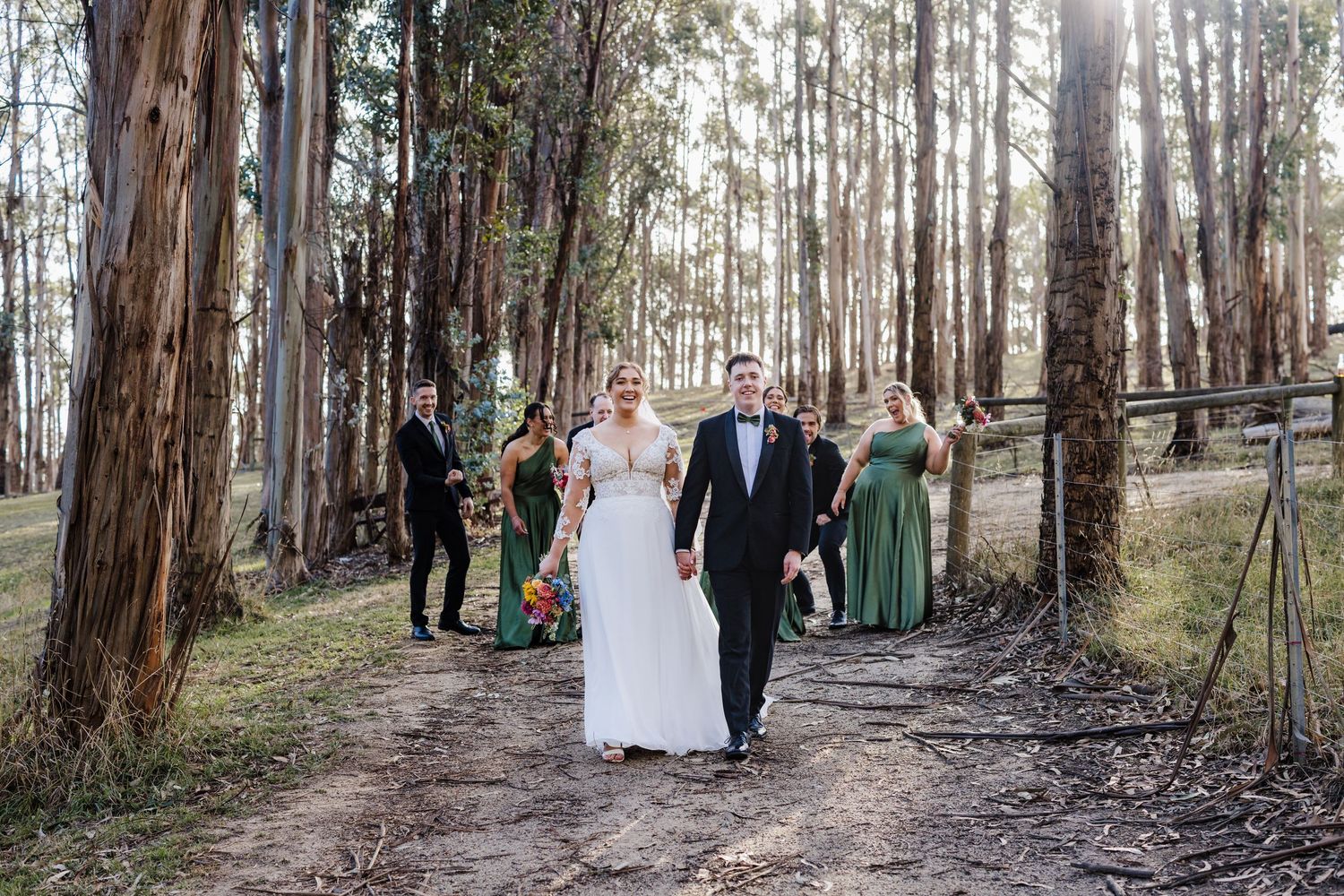 A wedding party stands in a serene forest setting surrounded by tall eucalyptus trees during an outdoor ceremony.