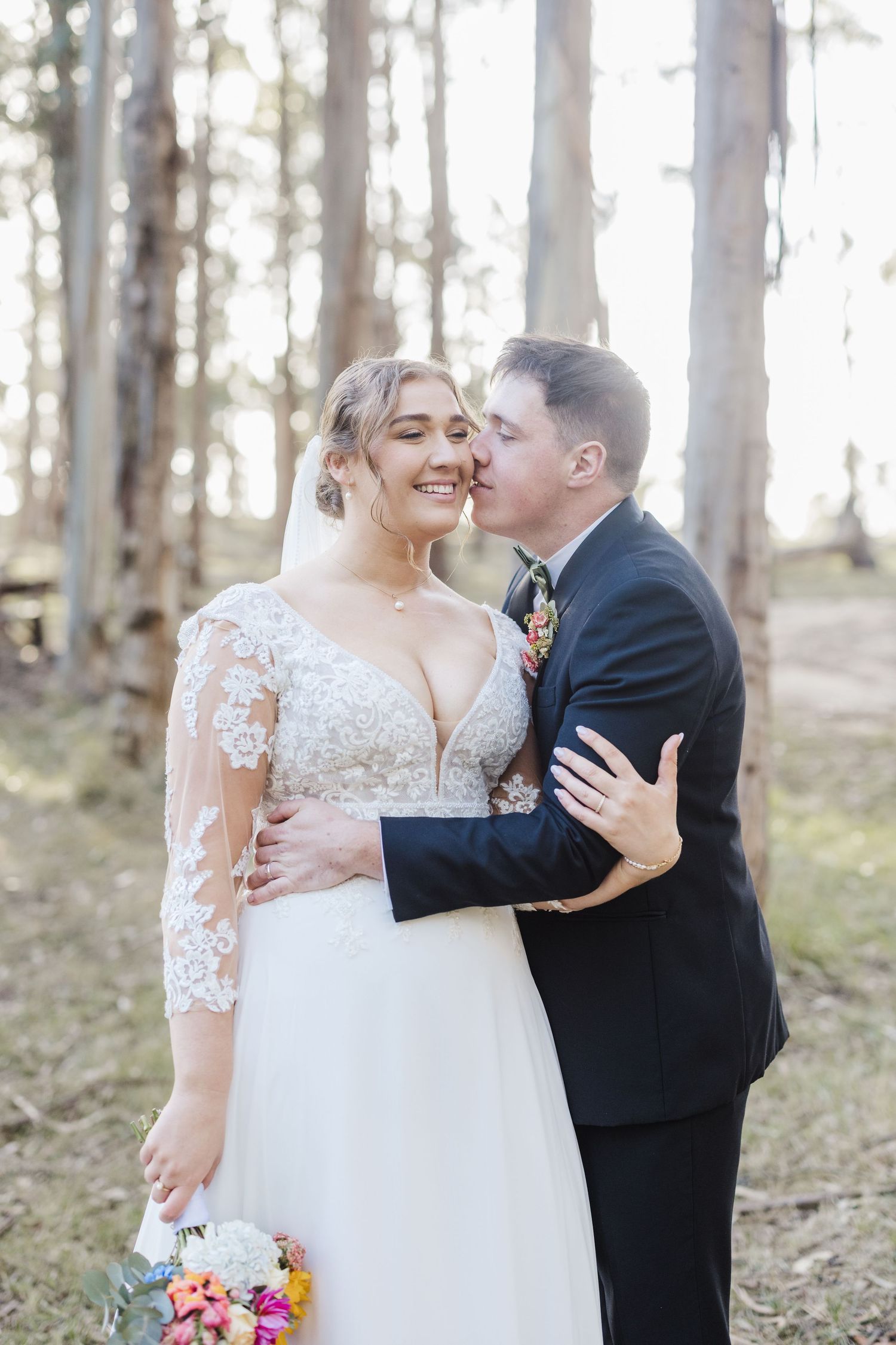 A romantic wedding moment captured in a wooded setting with soft natural lighting and a beautiful floral bouquet.