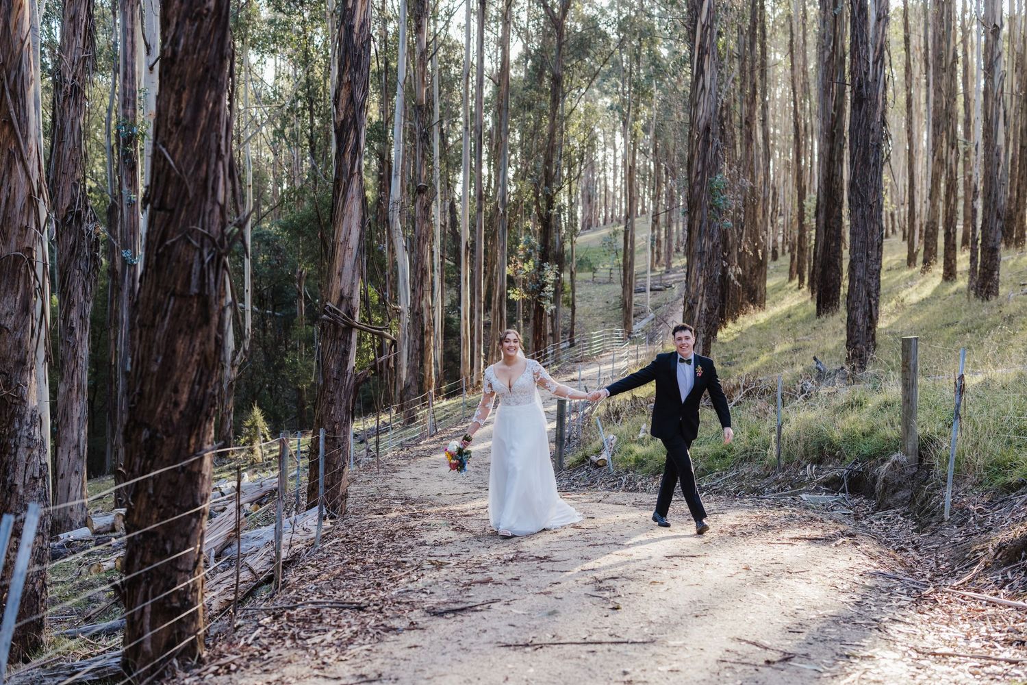 People walking through a sunlit forest path with tall trees casting long shadows on the ground.