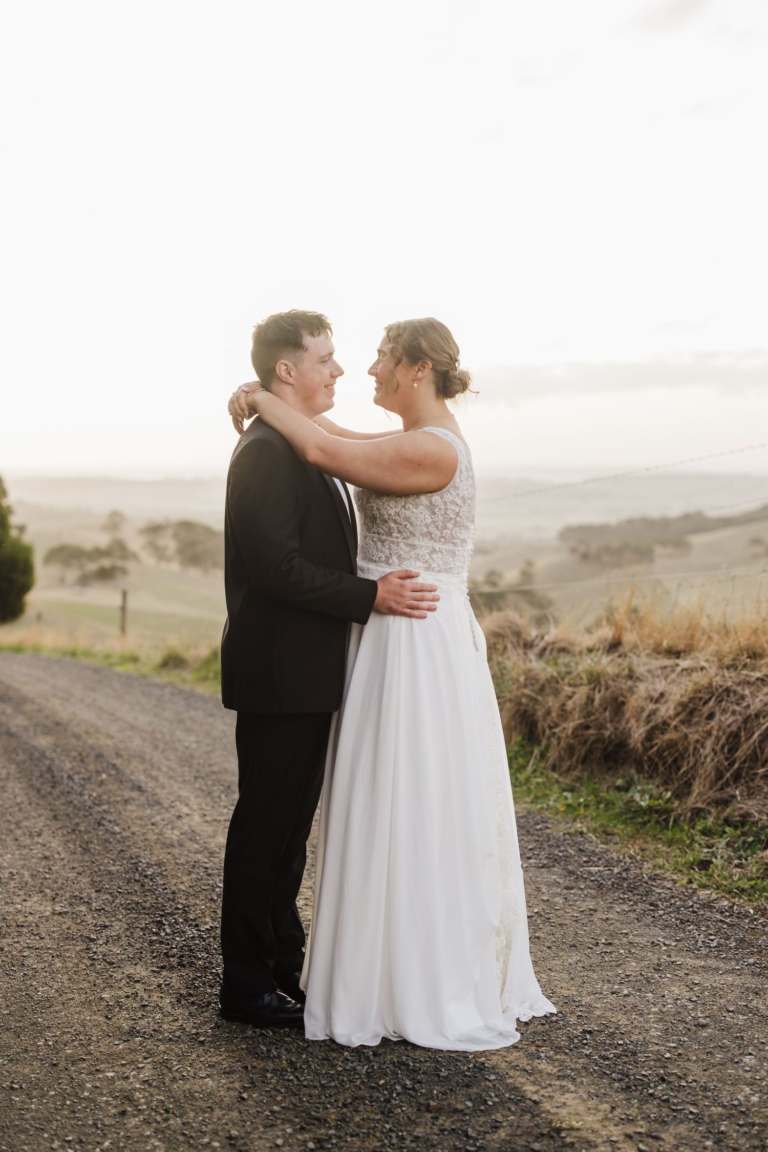 Newlyweds embrace tenderly on a scenic hilltop path during golden hour.