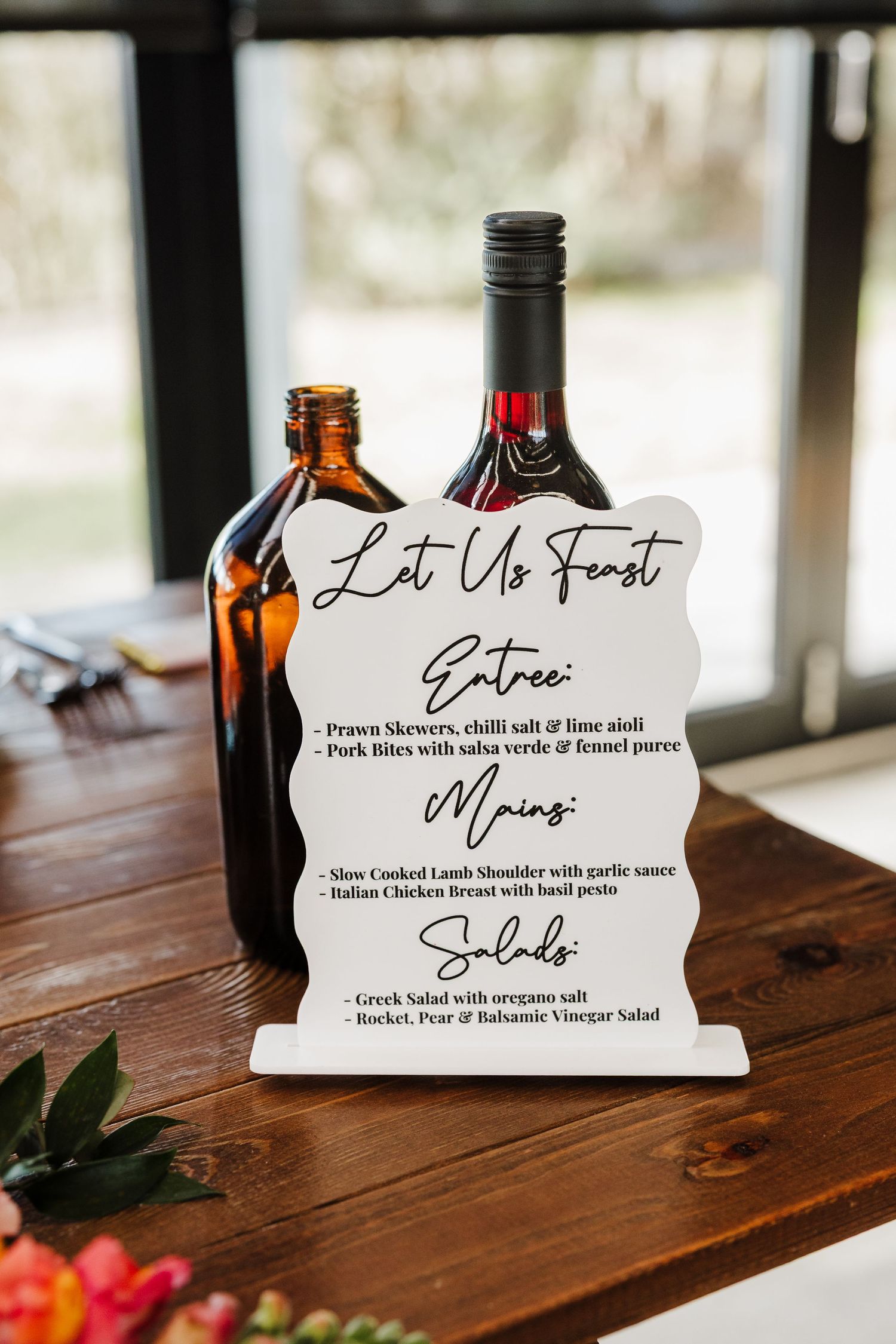 Wedding menu cards and wine bottles displayed on rustic wooden table with elegant calligraphy text.