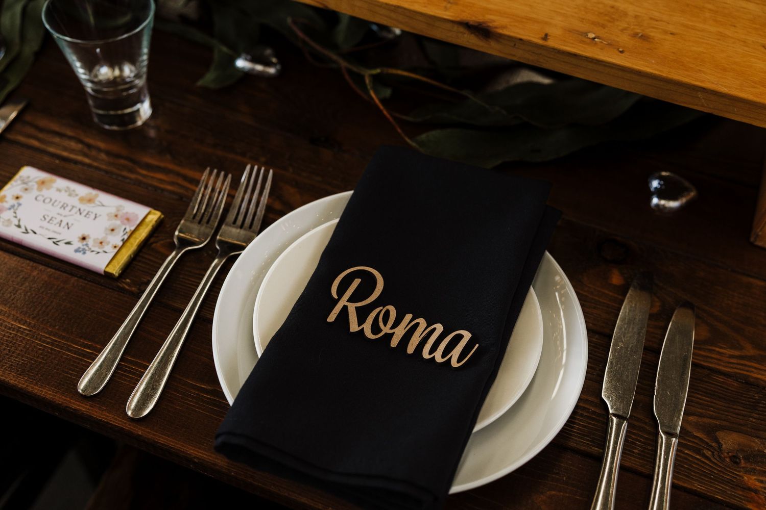 Restaurant table settings with white plates, silverware, and glasses on dark wooden surfaces in elegant lighting.