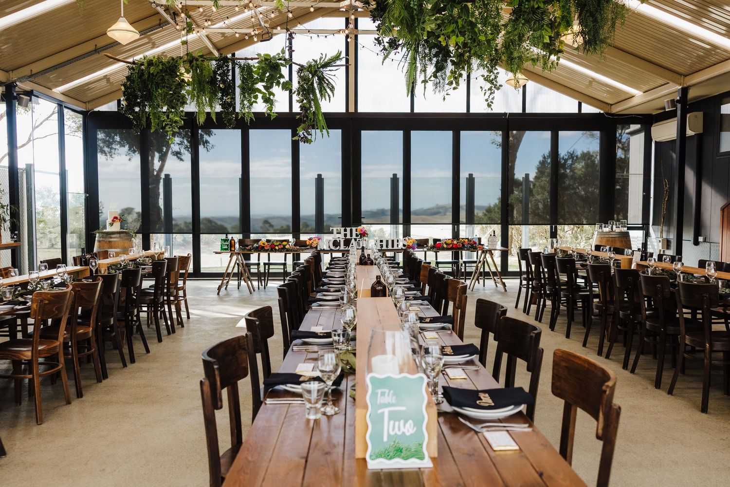 A panoramic view of an outdoor covered restaurant patio with wooden tables and chairs overlooking a waterfront.