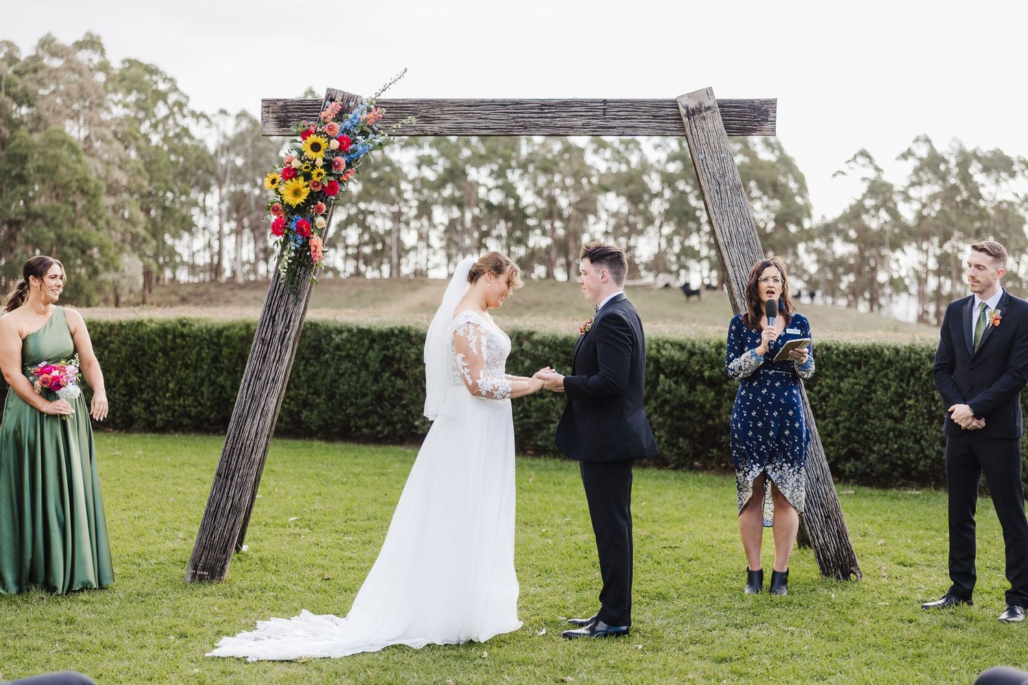 Outdoor wedding ceremony setup with wooden arch and chairs on a grassy lawn surrounded by trees.