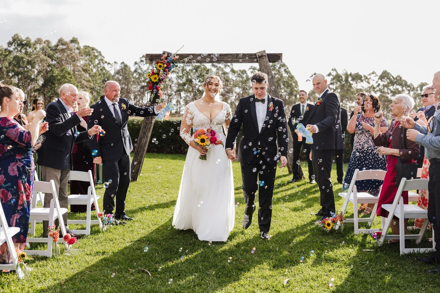 Wedding guests shower newlyweds with confetti during an outdoor garden ceremony celebration.