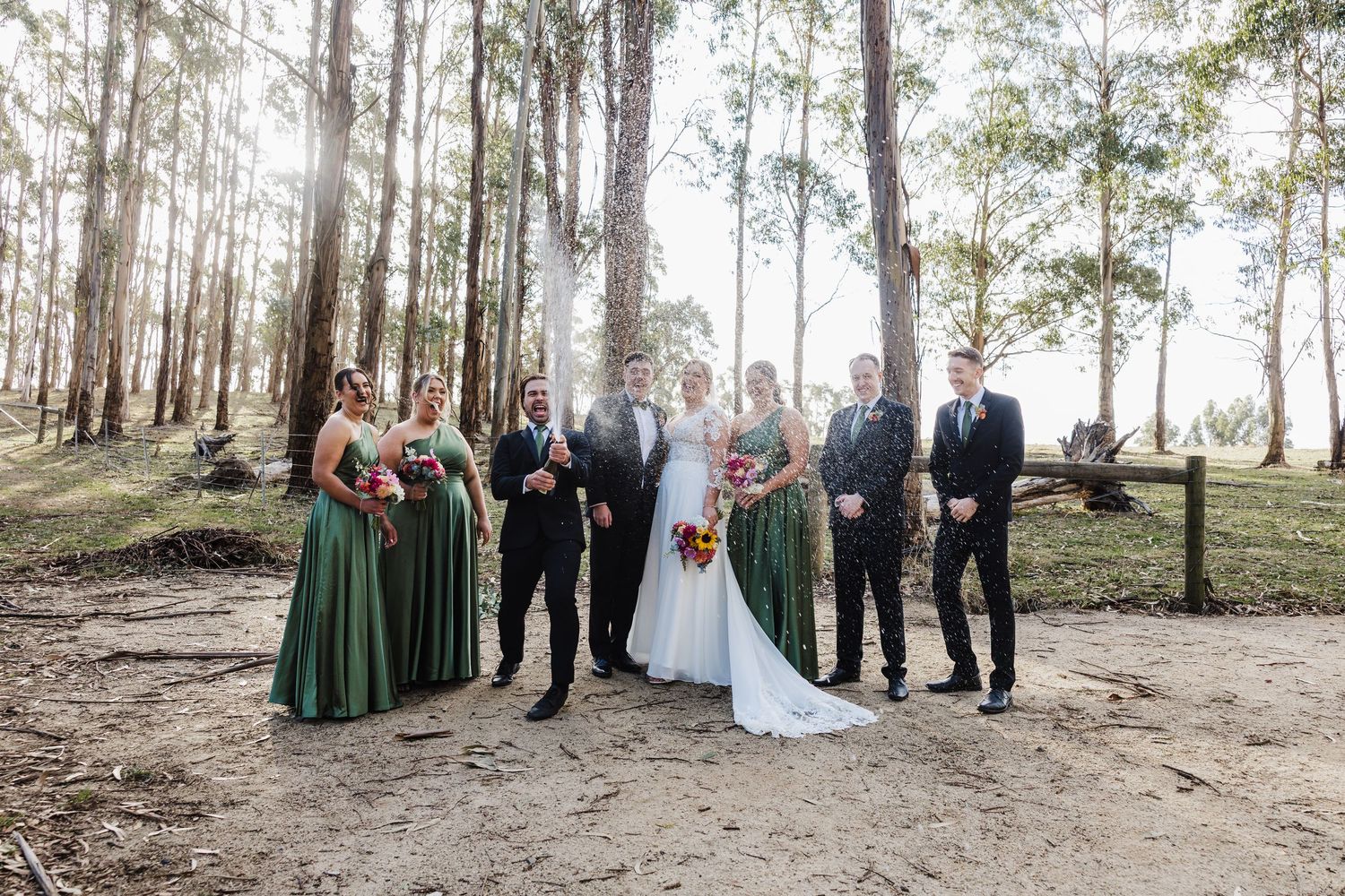 Wedding party poses together in a scenic forest setting with tall trees and natural lighting.