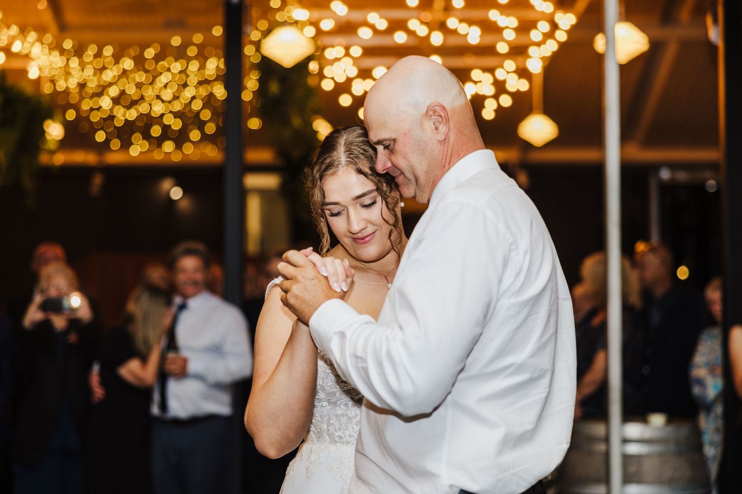 A couple shares a romantic dance under twinkling lights at an evening reception.