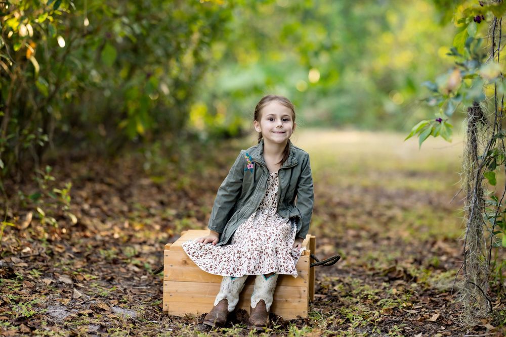 A young child sits on a wooden swing hanging from a tree branch in a lush autumn forest setting.