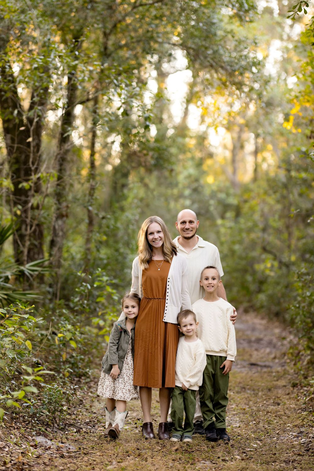 Family portrait session in a sunlit wooded area with autumn foliage creating a natural outdoor backdrop.