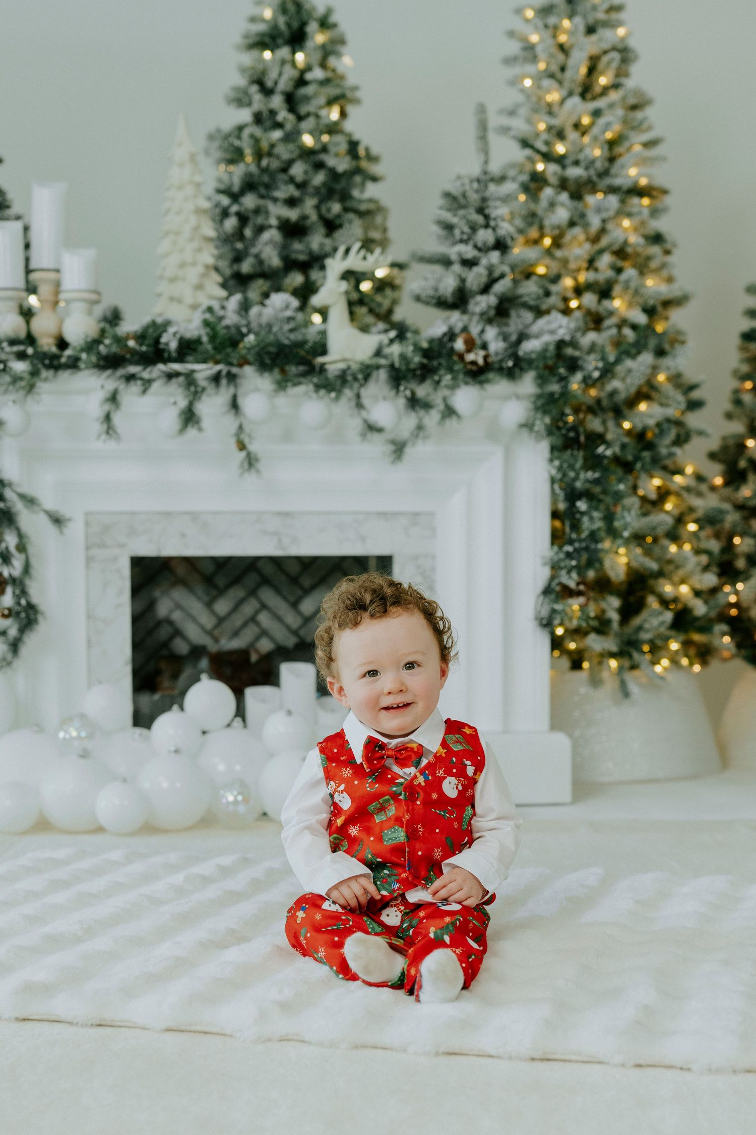 A festive holiday scene with a decorated Christmas tree, white fireplace mantel, and cozy white blankets on the floor.
