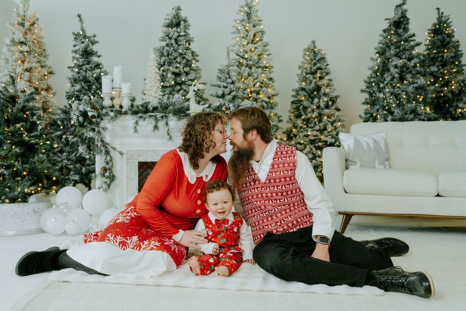 Family wearing festive red and white holiday outfits lies on floor near decorated Christmas tree.