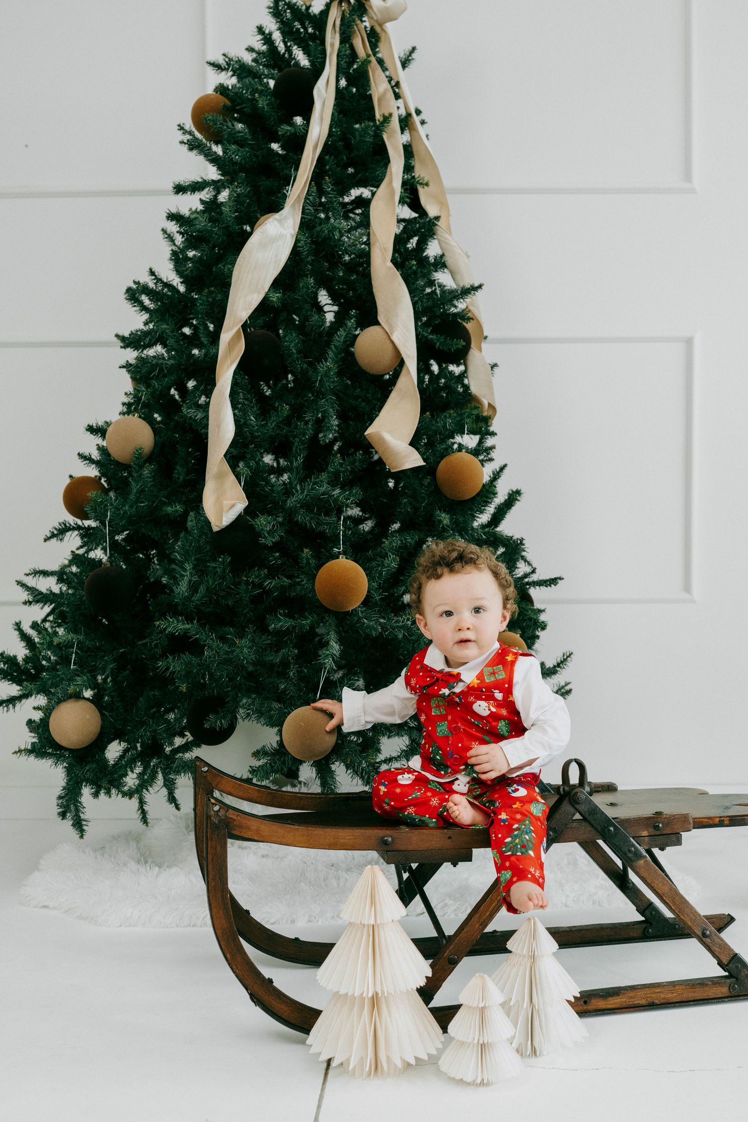 A decorated Christmas tree stands behind a vintage wooden sleigh with festive holiday decorations and ornaments.