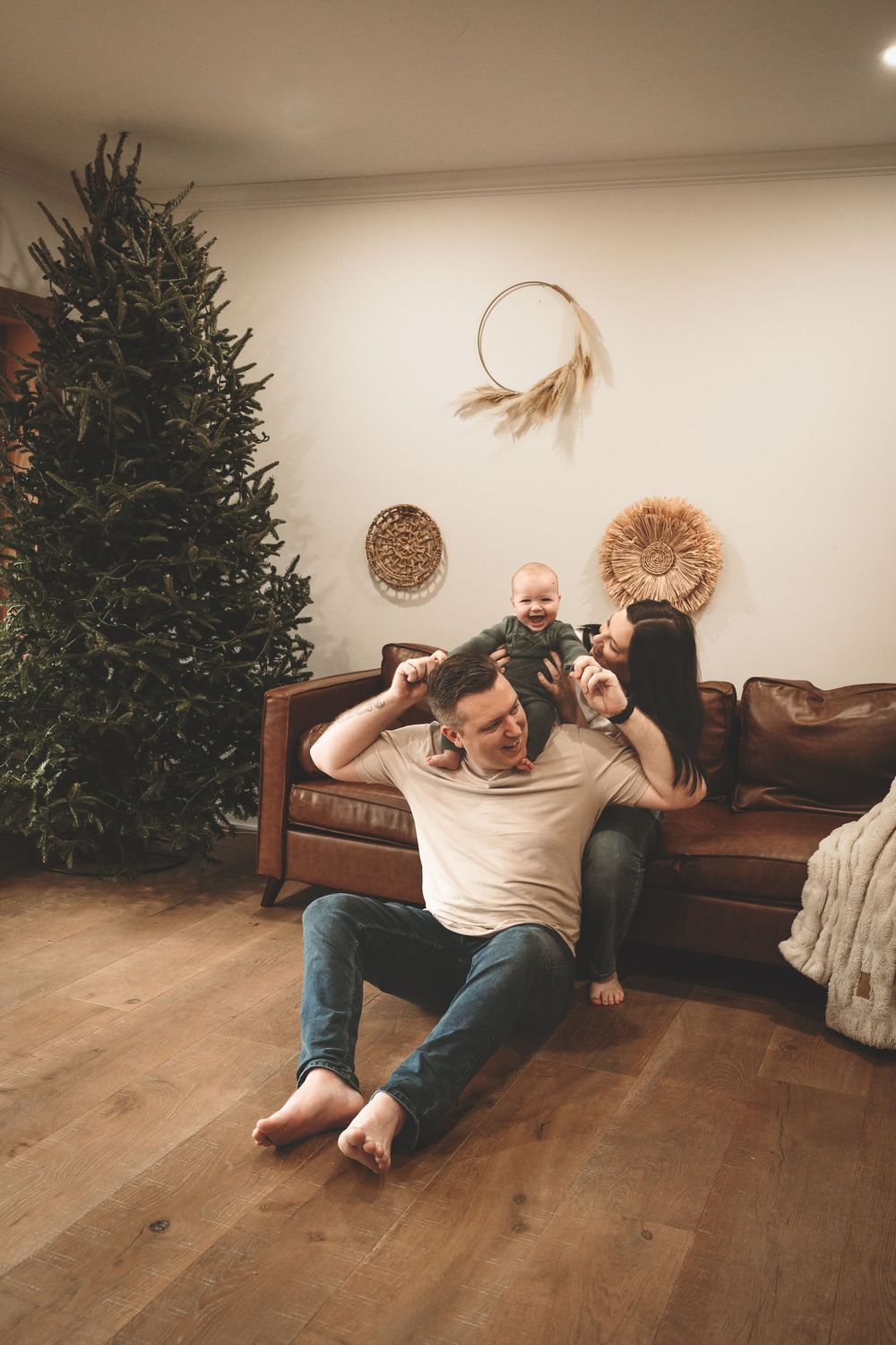 A series of playful moments captured near a Christmas tree and brown leather couch on hardwood floors.